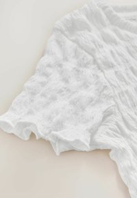 Witte, gestructureerde stoffen top met een rimpelende mouwrand; heeft een geplisseerd oppervlaktedesign en een ontspannen, vloeiende uitstraling.