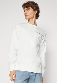 Hvid sweatshirt med rund hals, lange ærmer og ribbede manchetter. Har "GANT 1949" logo i sort på det øverste venstre brystområde.