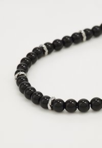 Collier de perles noires avec des perles rondes brillantes entrecoupées d'accents en argent. Le design est symétrique et lisse au toucher.