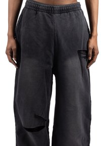 Črne, široke hlače z elastičnim pasom, z raztrganim rezom na stegni, izdelane iz mehke tkanine z mat zaključkom.