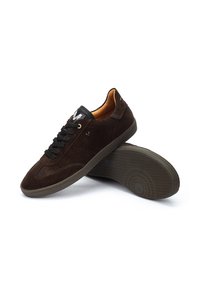 Zapatillas de ante marrón oscuro con lengüeta de cuero negro, puntera redonda y suela de goma texturizada con un patrón circular.