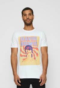 Hvid bomulds T-shirt med et grafisk tryk af David Bowie i kraftige orange og blå farver, omkranset af et svajende mønster.