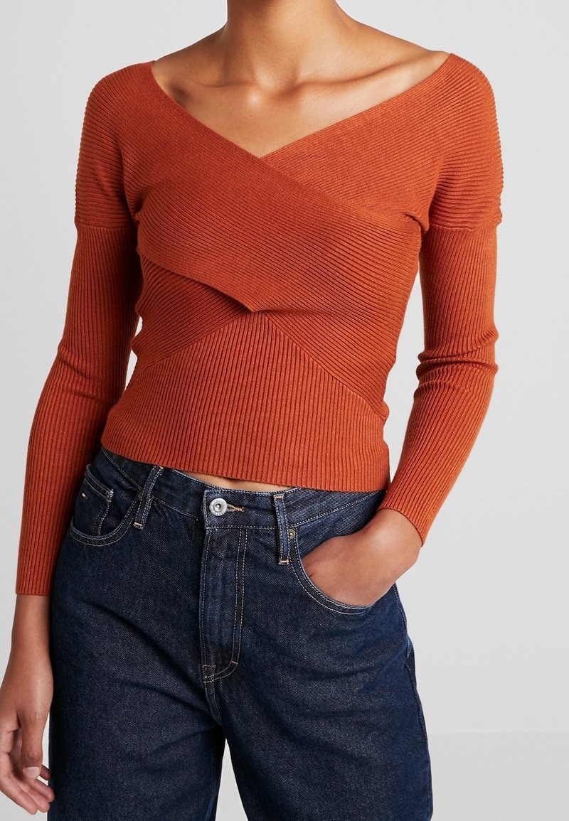 Haut à manches longues côtelé orange brûlé avec un design croisé et un décolleté épaules dénudées, associé à un jean denim foncé taille haute.