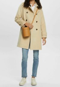 Beige dubbelknäppt kappa i ullblandning, med stora knappar. Matchad med ljusblå jeans och vita sneakers. Liten beige axelväska.