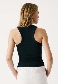 Juodas ribotuotas topas su lenktu nugariniu kirpimu. Pasirinktas prigludęs siluetas ir sklandus paviršius, derinamas su baltais džinsais, kuriuose matomas logotipo detalė.