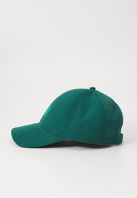 Casquette de baseball vert foncé avec un bord incurvé, fabriquée en tissu texturé, présentant des accents brodés et un logo sur le côté.