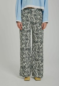 Pantaloni largi cu un imprimeu de șarpe alb-negru, având un material texturat. Asortați cu pantofi bej cu vârf ascuțit și o bluză scurtă de culoare albastră deschisă.