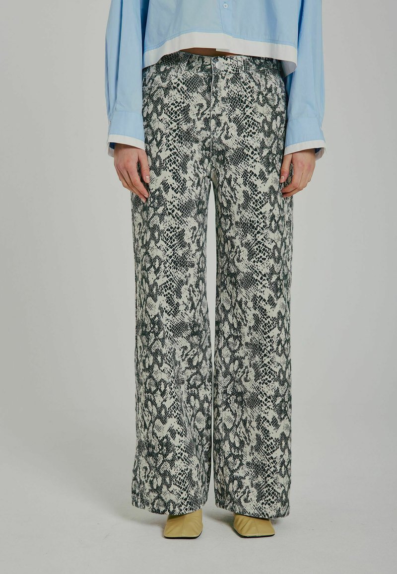 Pantaloni largi cu un imprimeu de șarpe alb-negru, având un material texturat. Asortați cu pantofi bej cu vârf ascuțit și o bluză scurtă de culoare albastră deschisă.