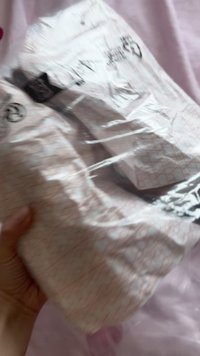 Ambalaj plastic alb cu un design de rețea roz, parțial deschis, dezvăluind un obiect în interior. O mână ține ambalajul împotriva unei suprafețe moi.