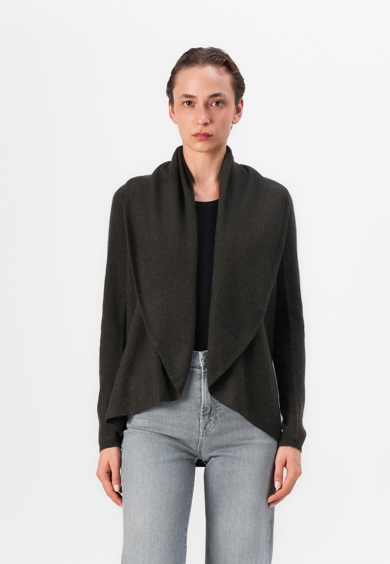 Cardigan aperto verde scuro realizzato in tessuto morbido con davanti drappeggiato, maniche lunghe e vestibilità rilassata, abbinato a jeans grigi a vita alta.
