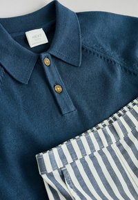 Polo bleu pour bébé avec boutons en bois et pantalon bébé rayé blanc et bleu, posé à plat sur une surface claire.