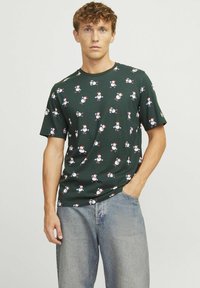 Grøn bomulds t-shirt med et gentaget snemand mønster i rød, hvid og blå. Korte ærmer og rund hals, parret med lyse denim.
