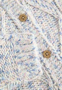 Cardigan en maille avec un fil pastel bleu et rose, des motifs texturés et un bouton décoratif en forme de fleur marron à l'avant.