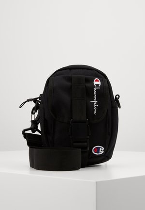 Sort kompakt Champion skuldertaske med justerbar rem, frontspænde, lynlåslommer og broderede logodetaljer.