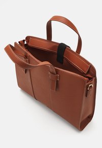 Sac fourre-tout en cuir marron avec doubles poignées et coutures blanches contrastées, comportant un compartiment zippé et deux poches extérieures.