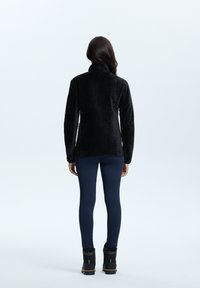 Pullover in pile nero con un motivo herringbone testurizzato, colletto alto e maniche lunghe. Abbinato a leggings blu navy e stivali neri.