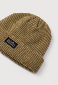 Ribbet strikket beanie hat i brune og grå nuancer med foldet kant og lille rektangulær sort mærke på hvid baggrund.
