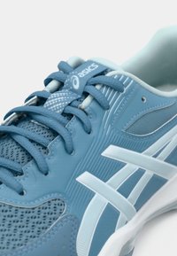 Μπλε αθλητικό παπούτσι Asics με κορδόνια, πλέγμα στην επάνω επιφάνεια, λευκές και ανοιχτό μπλε λεπτομέρειες, και επενδεδυμένος γιακάς εμφανιζόμενο σε κοντινή λήψη.