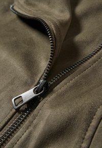 Olivgrön mocka med en delvis öppen metallblixtlås, med en texturerad yta och kontrasterande silverfärgade tänder och dragflik.