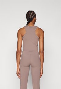 Femme aux cheveux tressés portant un haut sans manches mauve ajusté et des leggings taille haute assortis, vue de dos sur un fond uni.