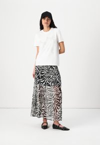 Vit bomull t-shirt med glittrande rosettdesign, kombinerad med en lång, genomskinlig, svart och grå nederdel med blommönster och svarta ballerinaskor med öglor.