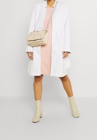 Biały płaszcz, jasnoróżowa sukienka, beżowa torebka na ramię z pikowanym wzorem oraz kremowe botki do kostki. Minimalistyczny i nowoczesny styl.