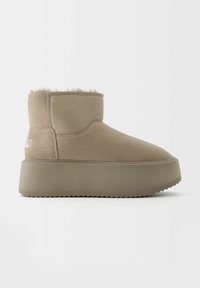 Béžové kotníkové boty vyrobené z měkké semišové kůže s podšívkou z umělé kožešiny, s tlustou, texturovanou podrážkou a kulatou špičkou.