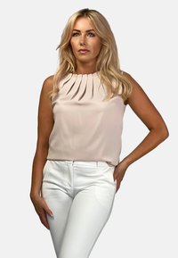 Jasno-różowa bezrękawnikowa bluzka z plisowanym dekoltem, w zestawie z białymi dopasowanymi spodniami. Gładki materiał, minimalistyczny design, brak widocznych wzorów.