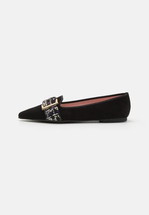 Chaussure plate noire à bouts pointus avec bride en tweed multicolore et boucle rectangulaire dorée sur fond blanc uni.