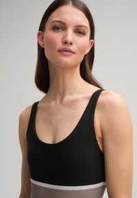 Maillot de bain bicolore noir et beige avec un décolleté en scoop et des bretelles fines, présentant une bande d'accent blanche horizontale à la taille.