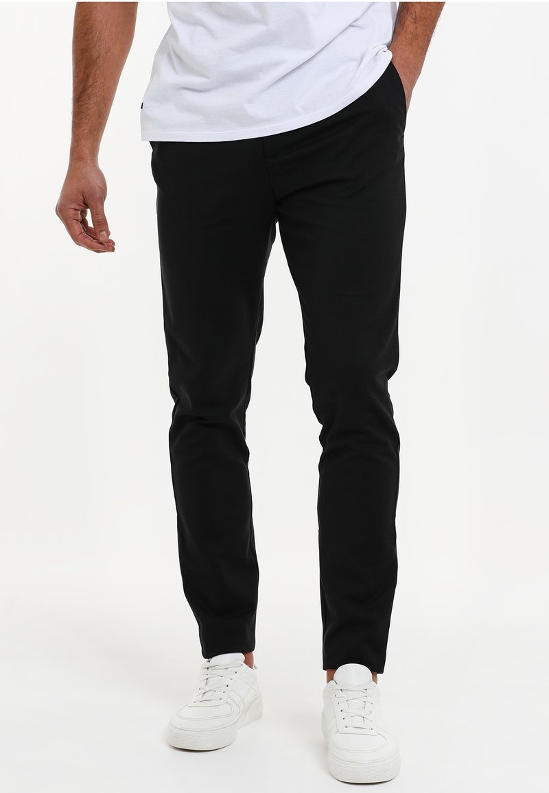Black tapered pants featuring a smooth fabric and side pockets, paired with white sneakers for contrast.