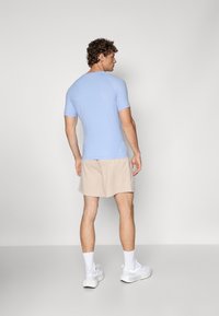 Himmelblaues kurzärmeliges Sportshirt mit einer figurschmeichelnden Passform, kombiniert mit beigen Shorts, getragen mit weißen Sportschuhen und Crew-Socken.