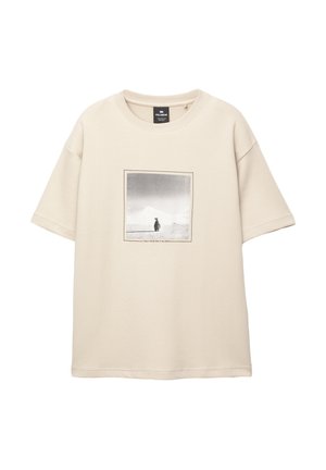 Beige cotton T-shirt with short sleeves, featuring a rectangular monochrome print of a person against a landscape. Text below print included.