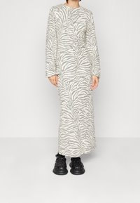 Sukienka z długim rękawem w kolorze kremowym z szarym wzorem zebry, o dopasowanym kroju i teksturowanej tkaninie. Zestawiona z czarnymi tkanymi butami.