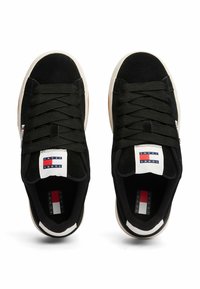 Par de zapatillas negras de corte bajo con cordones gruesos, suelas blancas y el logo de Tommy Jeans en la lengüeta y las solapas laterales, mostradas desde arriba.