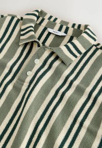 Polo en maille texturée vert et crème avec des rayures verticales, un col et deux boutons blancs sous l'encolure.