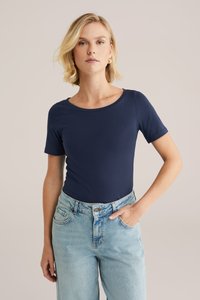 Marineblaue Kurzarmbluse mit Rundhalsausschnitt, aus glattem Stoff, kombiniert mit hellblauen hochgeschnittenen Jeans. Schlichtes, enges Design.