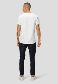 T-shirt en coton blanc à manches courtes et col rond, porté avec un jean en denim foncé et des baskets blanches. Forme carrée et texture lisse.