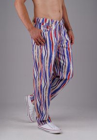 Mehrfarbige gestreifte Hose mit blauen, roten und weißen Mustern. Mit lockerer Passform, elastischem Bund und seitlichen Taschen. Kombiniert mit weißen Sneakers.