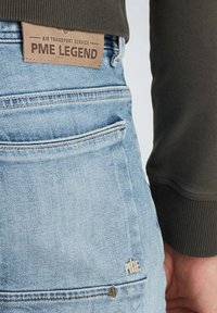 Vaqueros de mezclilla azul claro con una etiqueta de cuero marrón con la inscripción "PME LEGEND". Presenta un bolsillo trasero con costuras sutiles y detalle del logo.