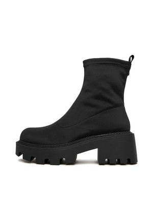 Zwarte enkelboot met chunky lugzool, blokhak, glad bovenmateriaal en een trekband aan de achterkant, getoond in profiel op een witte achtergrond.