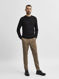 Black long-sleeve sweater, beige tapered trousers, and black shoes. Smooth texture with a classic fit, minimal design, and no visible patterns.