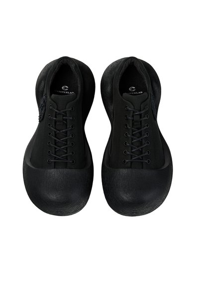 Paire de chaussures noires à lacets avec bouts de chaussures surdimensionnés et arrondis ainsi que semelles texturées, vues de dessus sur fond blanc.