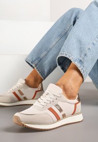 Baskets beige clair avec des accents marron, des panneaux texturés et des détails métalliques. Système de laçage avec une semelle blanche rembourrée et une semelle flexible.