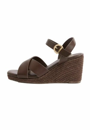 Rudos spalvos pleišto formos sandalai su kryžminėmis odinėmis juostelėmis ir aukso spalvos sagtimi, pintas virvinis platformos padas, atviri pirštai ir čiurnos dirželis.