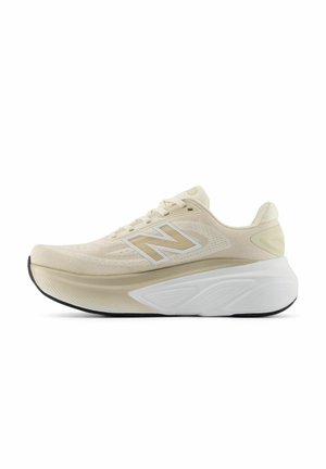 Beige en witte New Balance hardloopschoen met een gebreide bovenkant, dikke gevoerde tussenzool en zwarte buitenzool, weergegeven in zijaanzicht op een witte achtergrond.