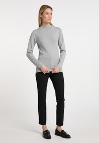 Világosszürke, hosszú ujjú felső, magas nyakkal, fekete, slim-fit nadrággal és fekete lófaragókkal párosítva. Az anyag lágy és kötött hatású.