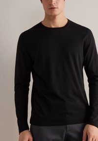 Maglietta nera a maniche lunghe realizzata in tessuto morbido, con scollatura rotonda e taglio aderente. Tessuto liscio con dettagli minimi.