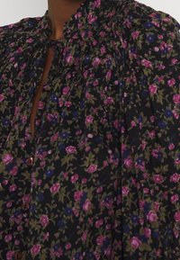 Blommig blus i svarttyg med rosa, blå och gröna blommor. Rynkad halsringning med knytning, knappstängning och mjuk textur.