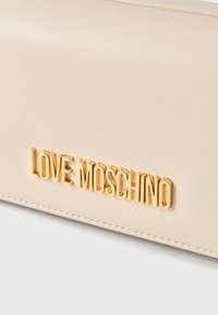 Υφή από δέρμα σε κρεμ απόχρωση με μεταλλικό χρυσό λογότυπο "LOVE MOSCHINO" και εμφανές ράψιμο κατά μήκος της άκρης.